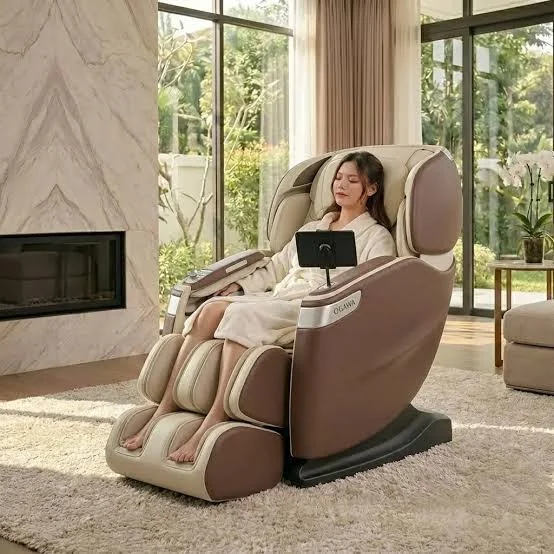 Brown and cream full-length massage chair with a tablet-style controller, placed on a shag rug in a bright living room beside a marble fireplace, with a person relaxing in a robe